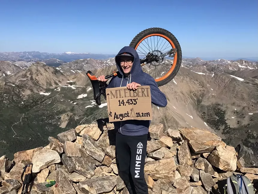 Caleb Kotter posed with his unicycle and a cardboard elevation sign on the Mount Elbert summit