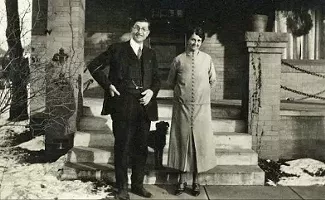 A man and woman pose in front of a house.