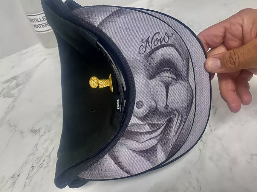 A comedy mask drawn in ballpoint on the bill of a cap.