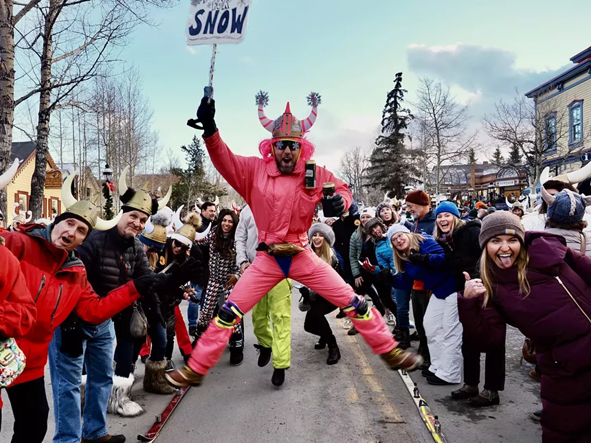 A man in a pink ski suit and Viking helmet jumping between shotski participants