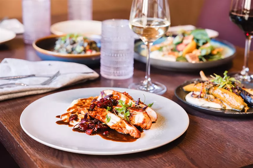 Toro's achiote-marinated turkey breast on a white plate next to glasses of wine and other dishes