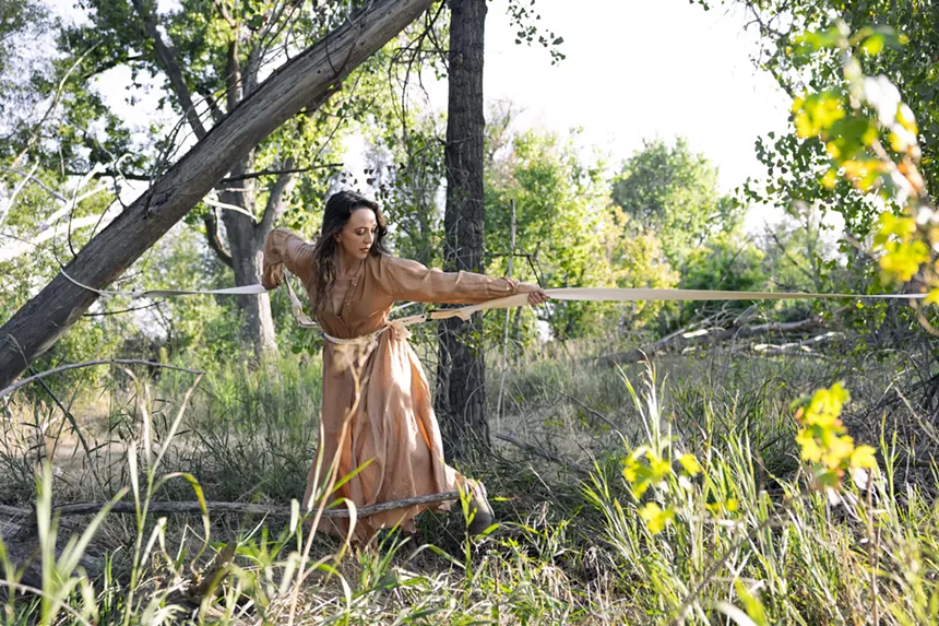 A woman wearing a brown dress pulls a rope in nature.