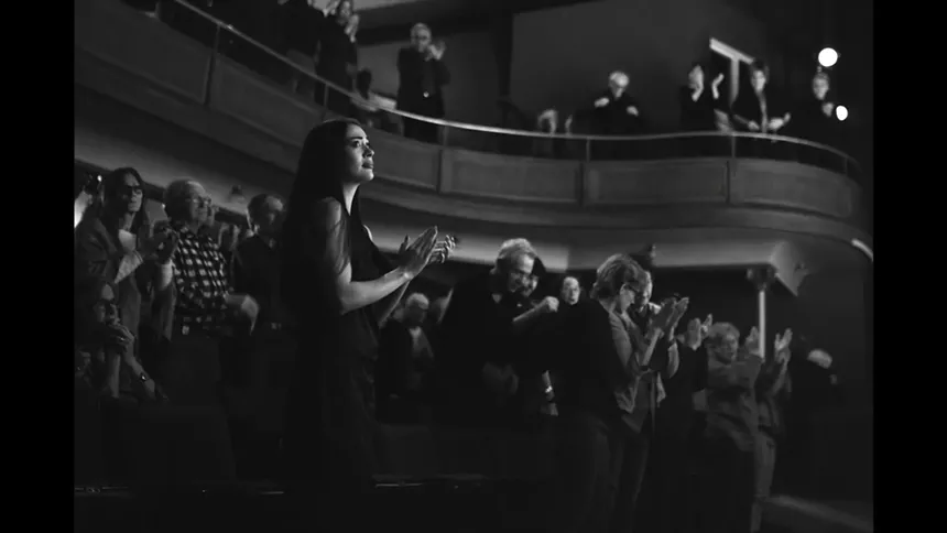 Black and white image of a woman standing and clapping in a theater.