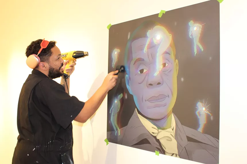 A black man uses a heat gun to hang vinyl on a wall.