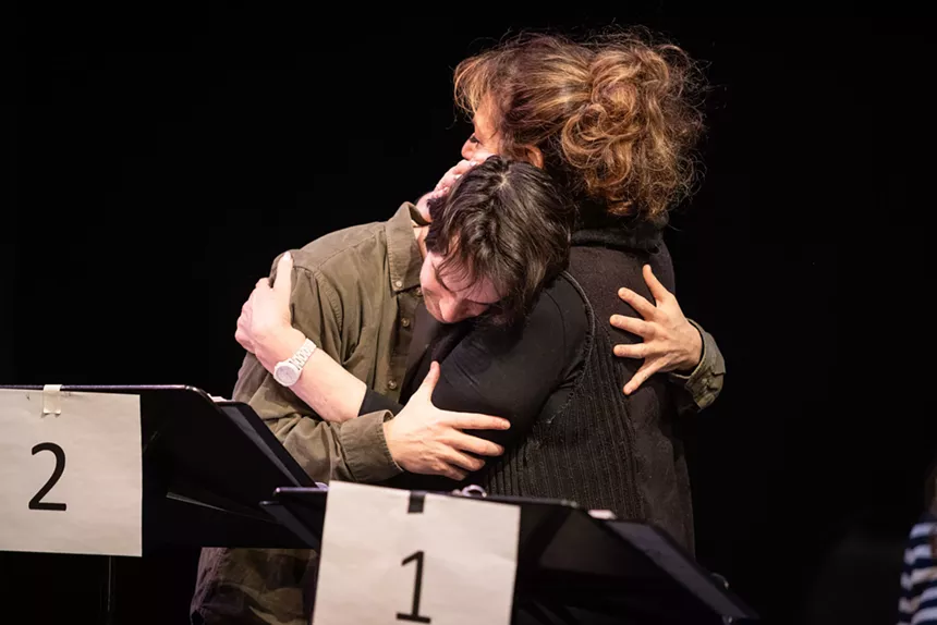Two people hug in front of a music stands.