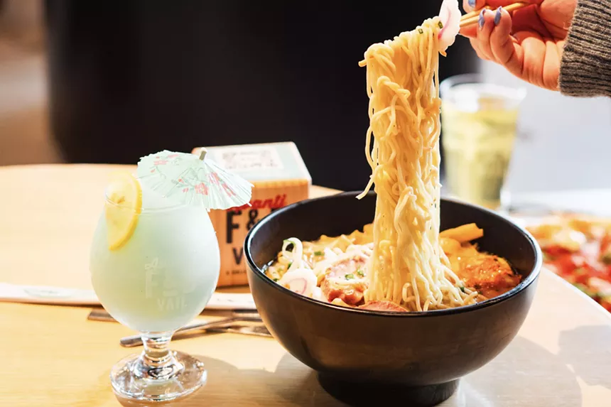 A person holding a pair of chopsticks, lifting up noodles from a Glo ramen bowl
