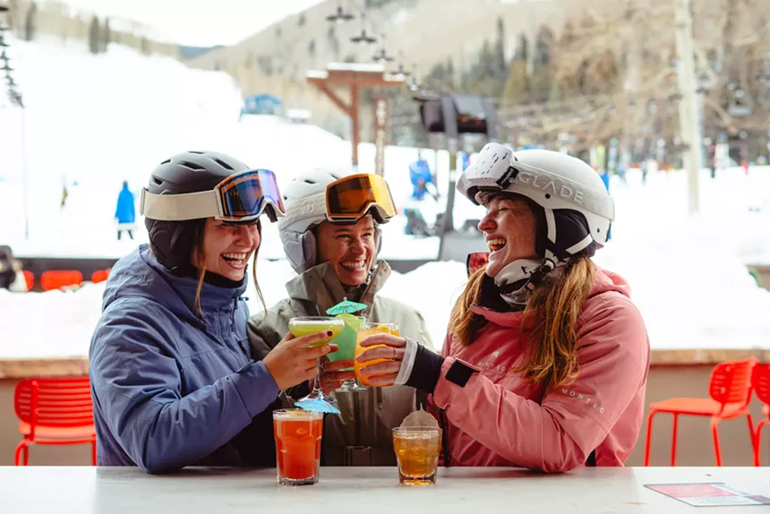 Three women in ski gear toasting cocktails on Avanti Vail's patio
