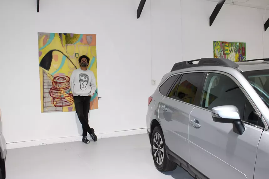 A Back man leans on his painting, which is surrounded by Subraus.
