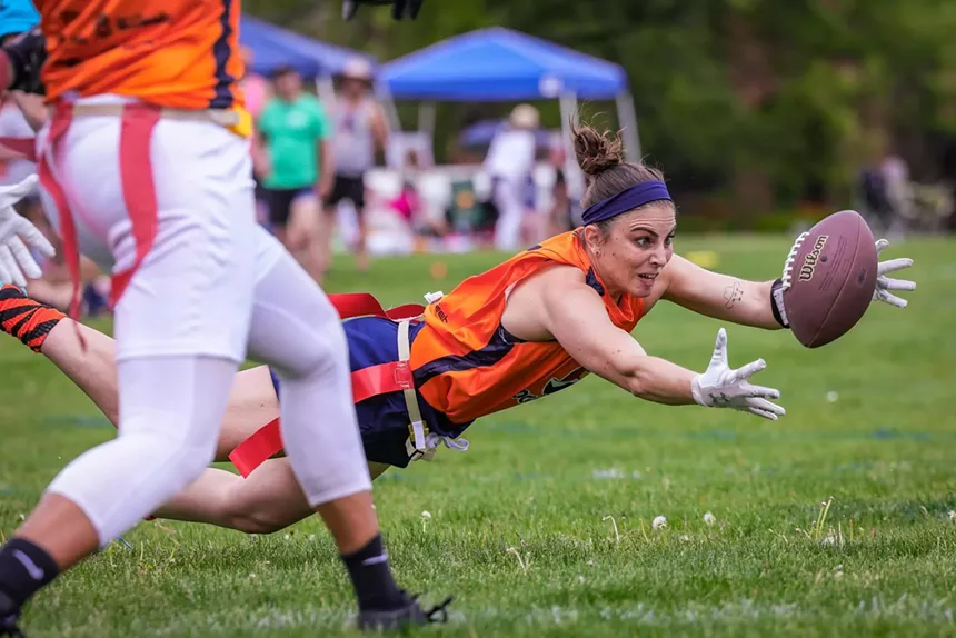 woman in an orange jersey, lunging to catch a football