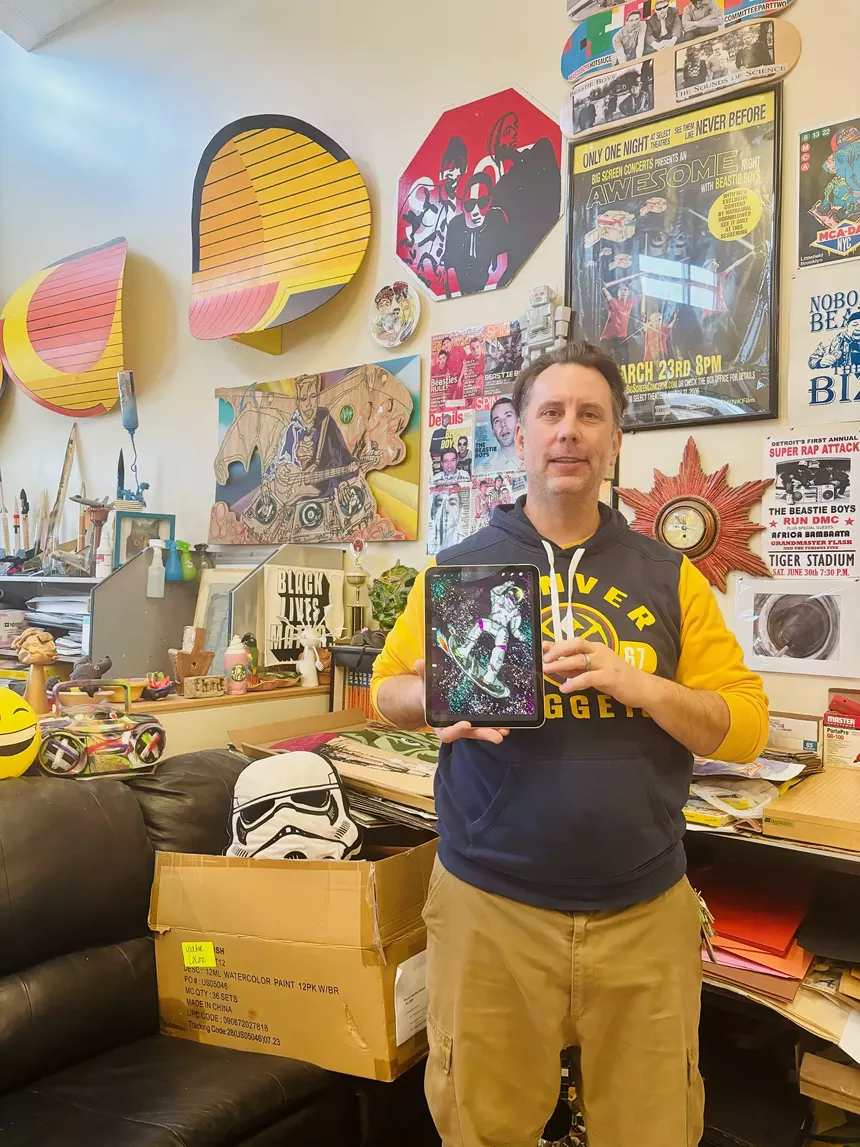 A man in a colorful art room holds a drawing of an astronaut