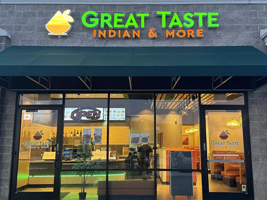 The exterior of Great Taste Indian & More, featuring large windows and a lighted sign
