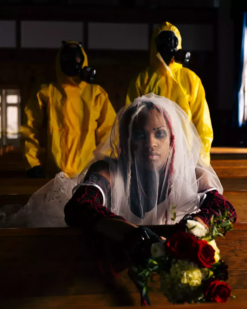 two people in hazmat suits stand around a bride in church pew