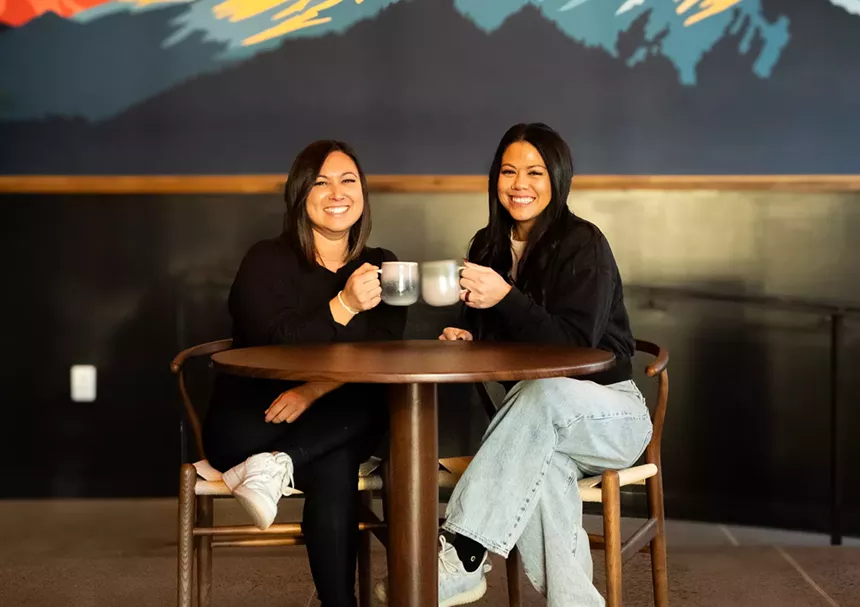 two women sitting at a table holding coffee mugs