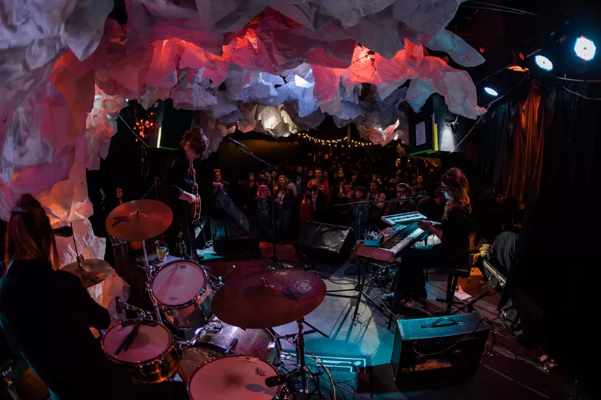 A photograph taken from behind the drummer during a band's performance on stage.