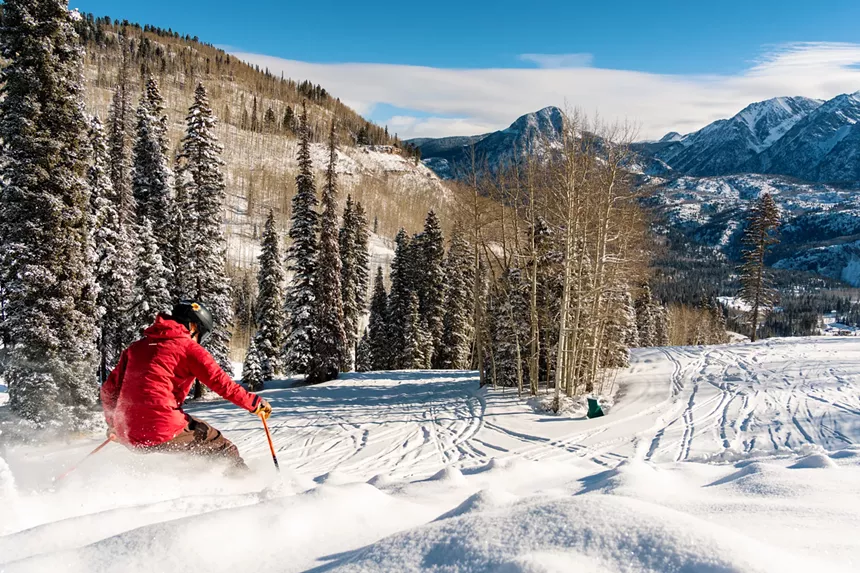 A person in a red coat skiing through powder at Purgatory Resort