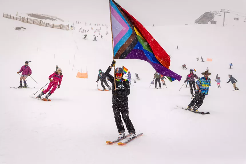 A skier holding a large Pride flag at A-Basin while backdropped by several other skiers
