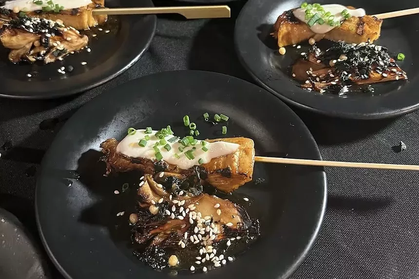 Grilled mushrooms and yuba on skewers, served on black plates