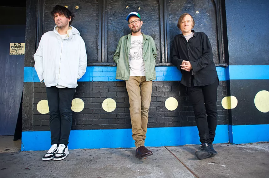 Bright Eyes' Conor Oberst, Mike Mogis, Nate Walcott stand on a sidewalk outside of a bar.