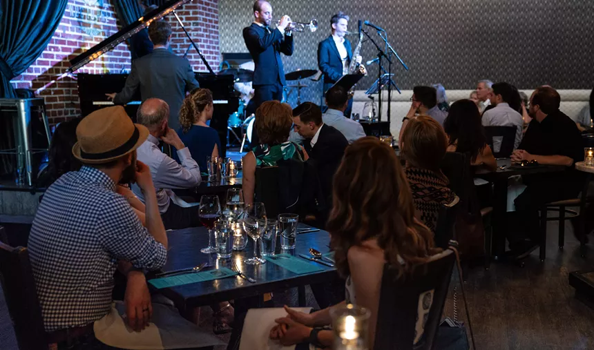 People sit at tables and listen to performers onstage.