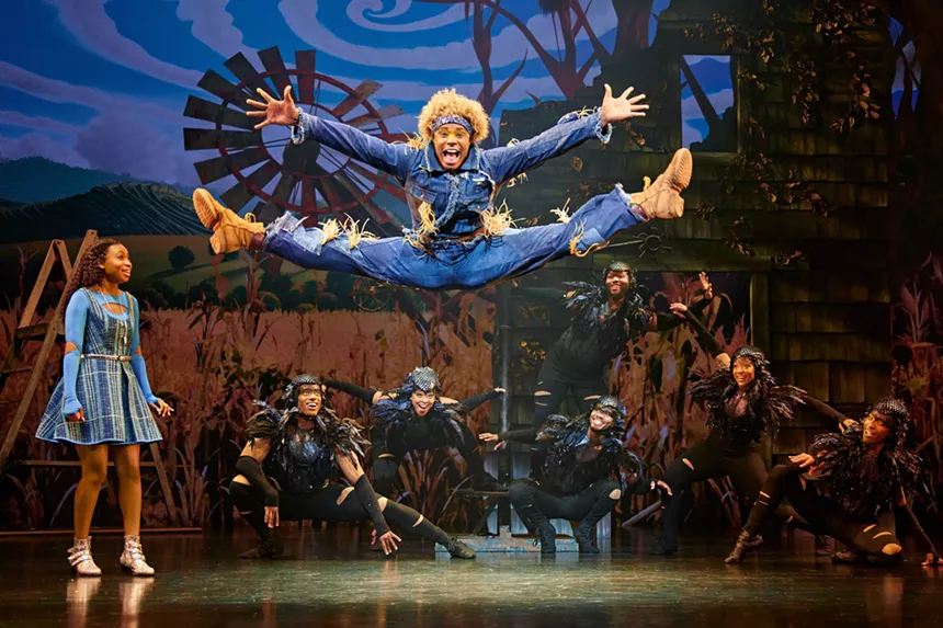 The Scarecrow does a spilt jump while Dorothy watches.