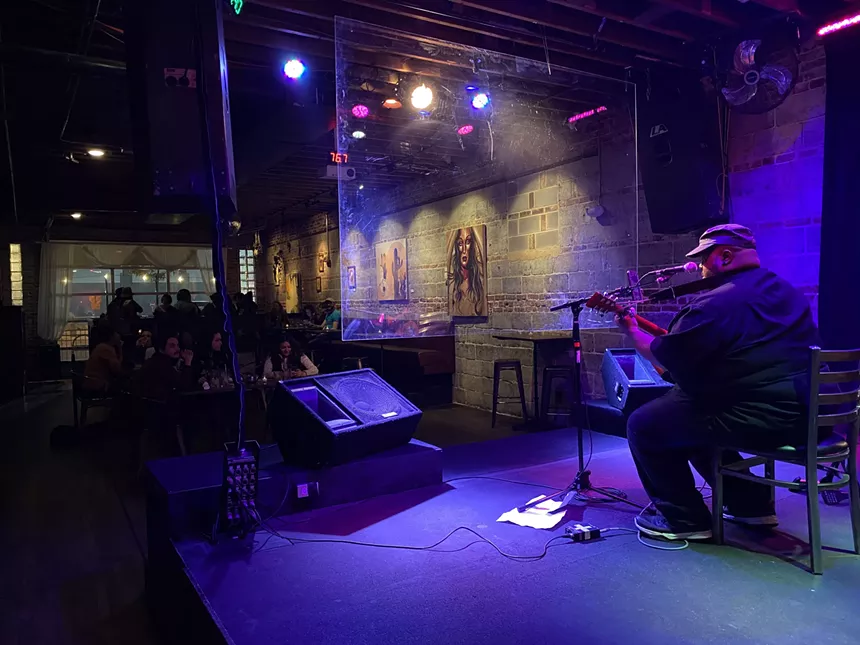 Someone playing guitar on an indoor stage with patrons watching from a table
