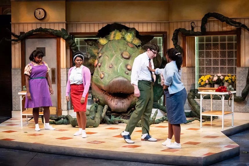 People stand in a flower shop near a massive plant puppet.