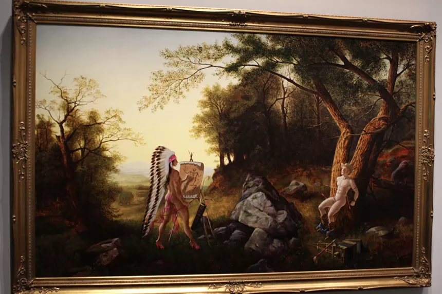 A native american paints a cowboy tied to a tree
