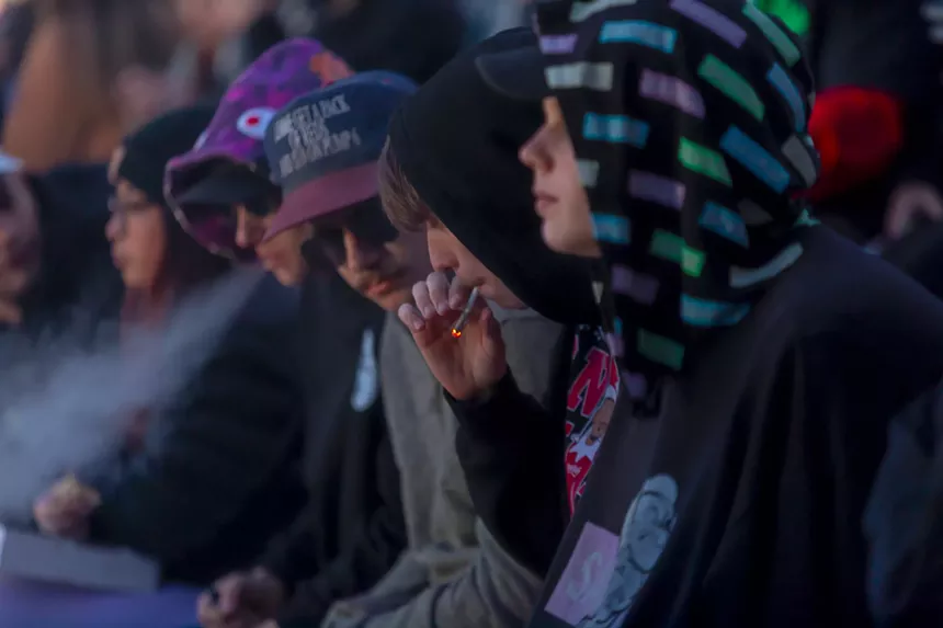 A photo showing multiple people huddled together with one smoking a joint.