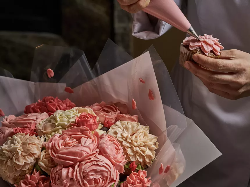 A chef piping an icing flower onto a cupcake