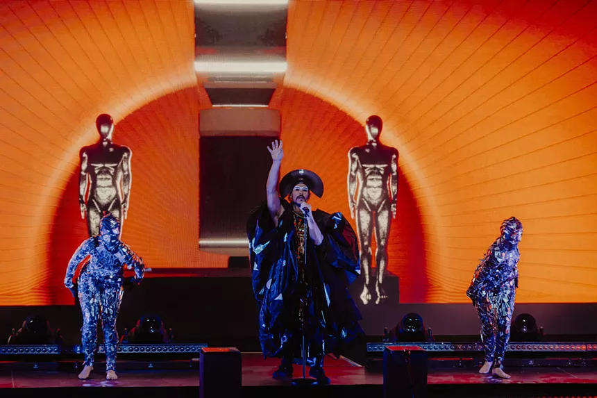 Empire of the Sun on stage with stage performers and visuals behind him.