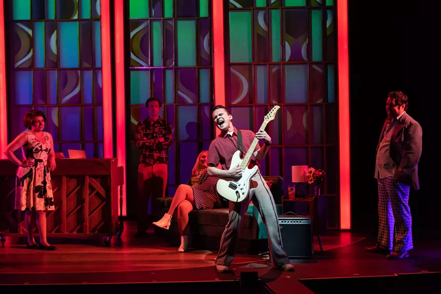 Onstage, a man plays guitar.