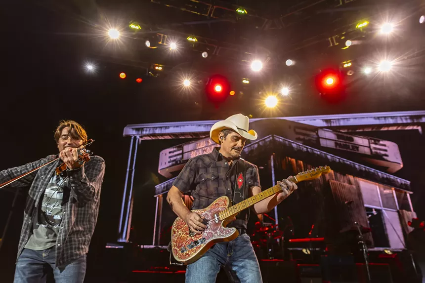 Brad Paisley on stage at Red Rocks with stage lights behind him and a violinist next to him.