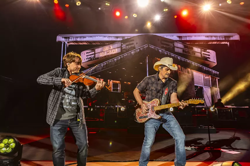 Brad Paisley on stage at Red Rocks with stage lights behind him and a violinist next to him.