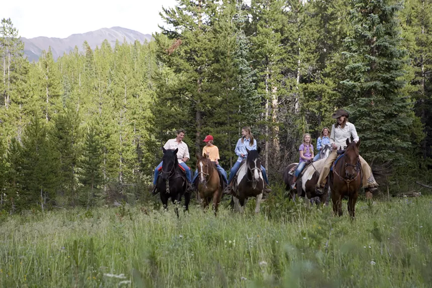 A group on a trail ride with Breckenridge Stables, backdropped by forests and mountains