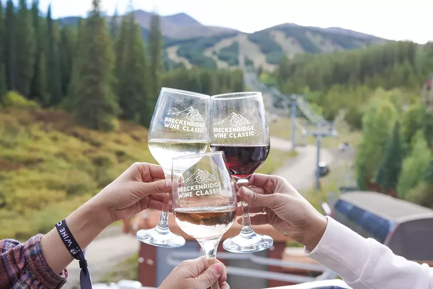 Three people toasting wine glasses with Breckenridge Ski Resort slopes in the background
