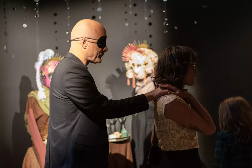 A blindfolded man is guided by hand through an art gallery.