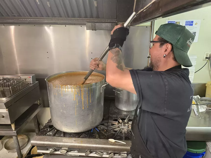 man stirring large pot of chile