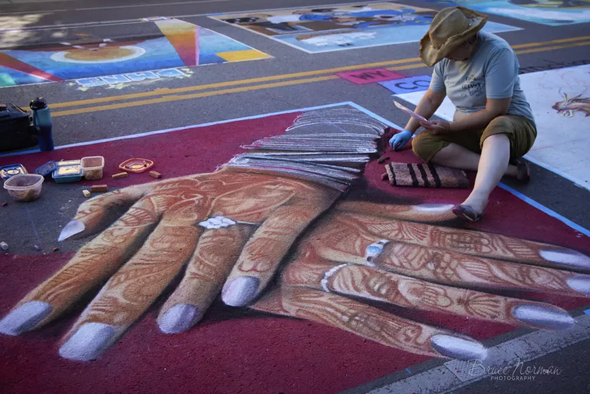 An artist uses chalk to create a street painting.