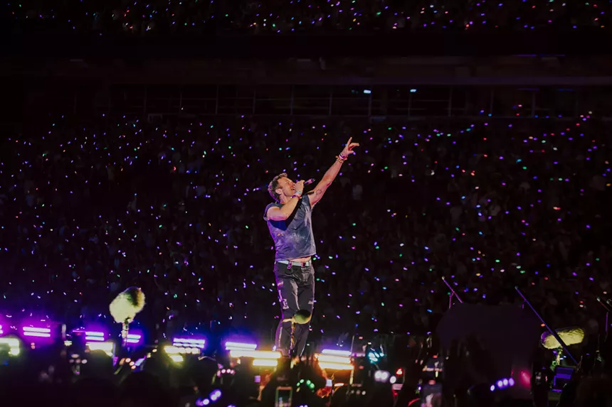 Chris Martin, lead singer of Coldplay, on stage at Empower Field at Mile High, embracing the crowd.