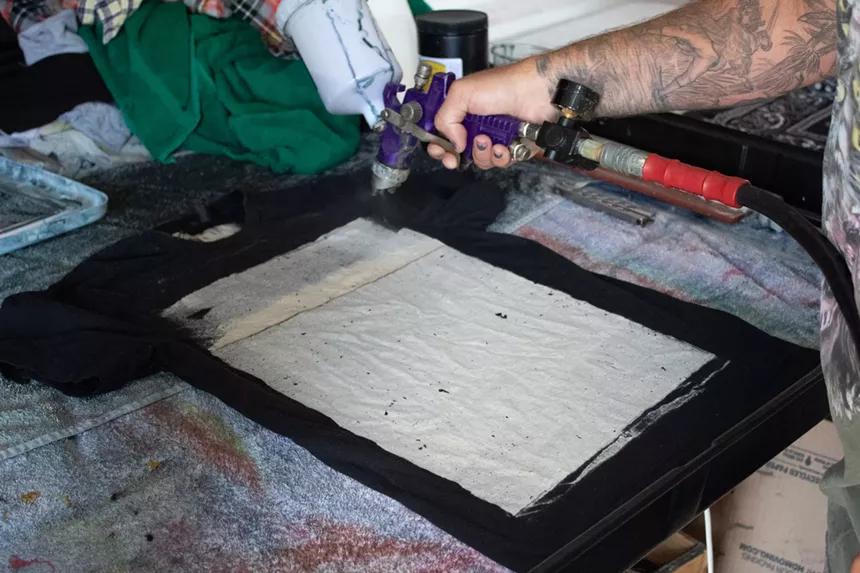 A hand sprays a clear dye onto a black shirt.