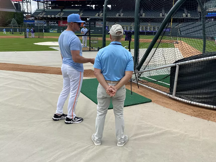 Baseball coach and announcer talk outside batting cage
