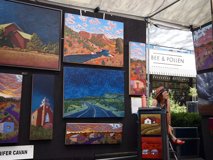 A woman sits near colorful canvases