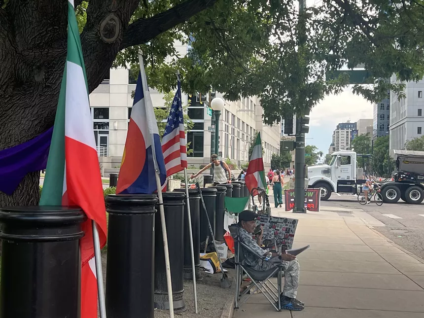 Man sits in lawn chair in front of flags on Denver street