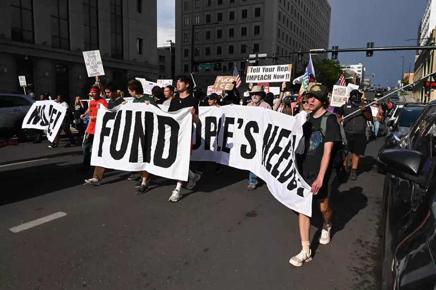 Protesters hold up a banner reading, "fund people's needs."