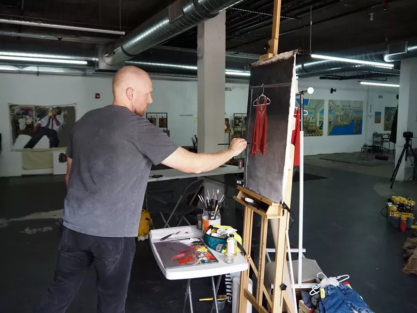 A man paints a picture of an orange dress
