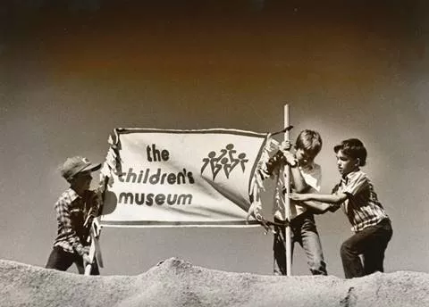 A black and white photo of kids holding up a sign that says "Children's Museum"