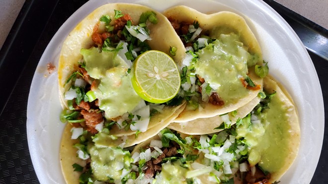 a plat of tacos topped with onions, cilantro and green salsa
