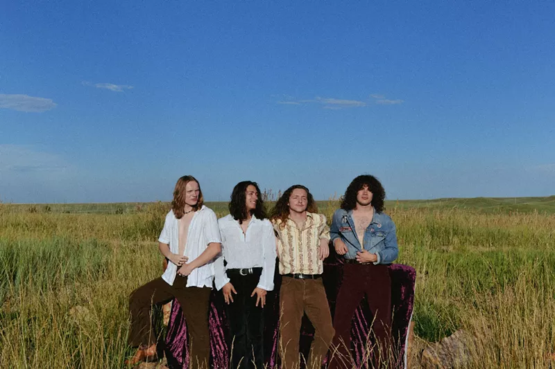 Image: four men standing in a field under blue skies
