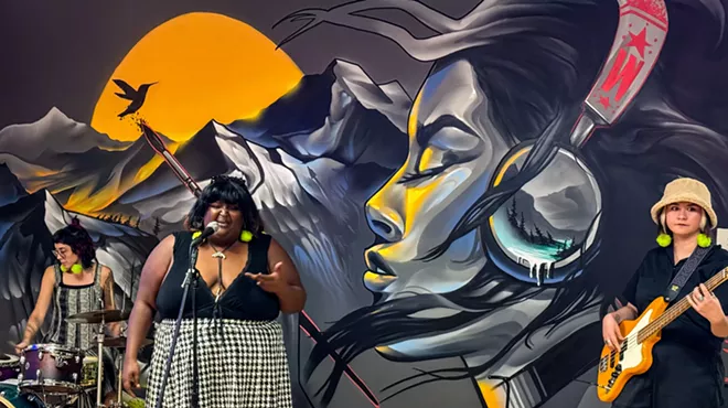 a drummer, singer and bassist performing in front of a mural