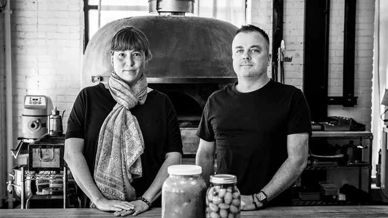 Image: black and white photo of a woman in a scarf next to a man in a black t shirt